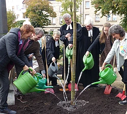 Mehrere Personen, unter anderem der Landesbischof Bedford Srrohm giessen einen frisch gepflanzten Baum an.