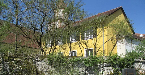 Eine bewachsene, alte Bruchsteinmauer begrenzt einen Friedhof hin zur Kirche.